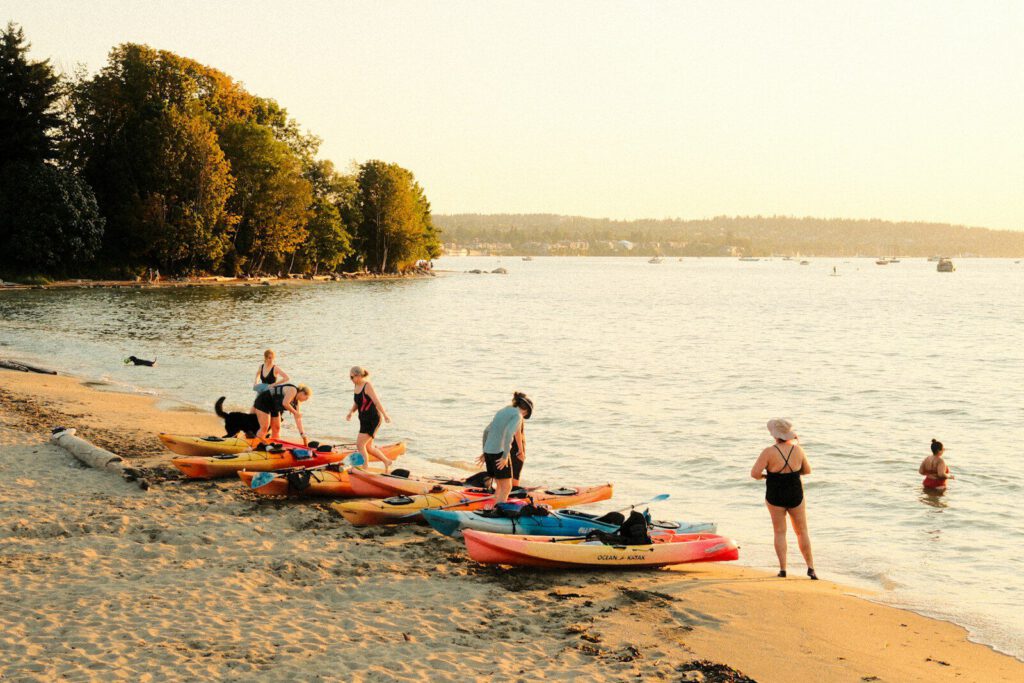 People with colorful kayaks on a sandy beach during the golden hour